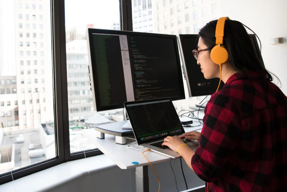 A developer wearing headphones writing code at a standing desk