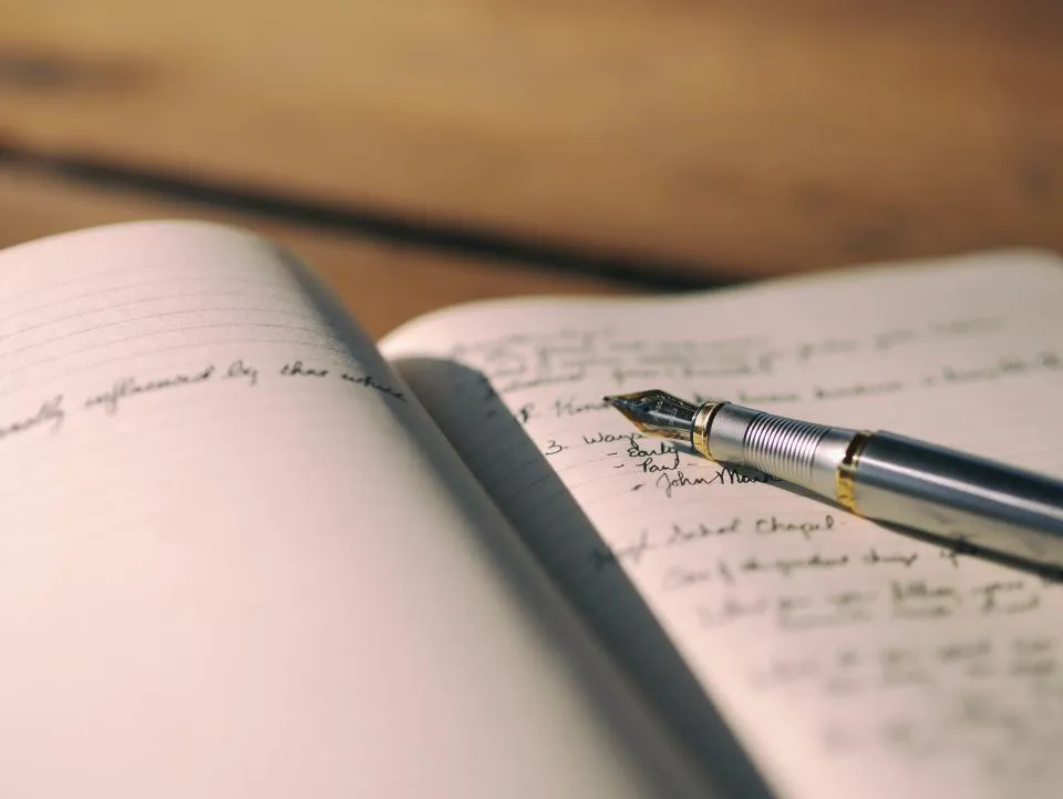 A fountain pen resting on an open notebook filled with handwriting